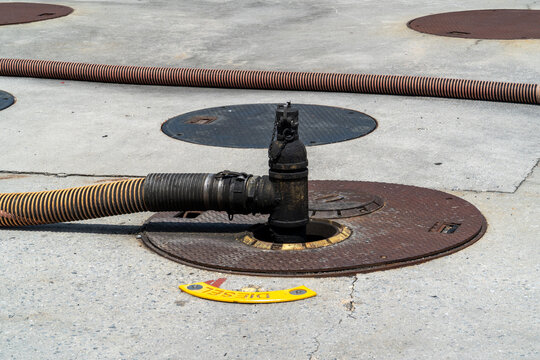 Diesel fuel delivery hose connected to underground storage tank access point on concrete pavement, emphasizing industrial and commercial liquid fuel transfer.