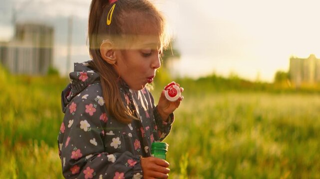 Young girl with hearing aids blowing soap bubbles in a sunlit grassy field, captured in dreamy slow motion with cinematic anamorphic lens flares