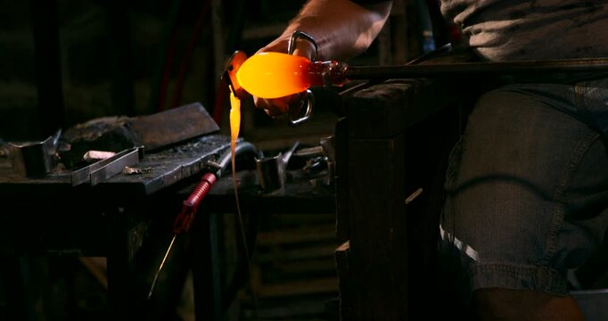 Close up of a glowing yellow piece of molten glass resting on a metal tool