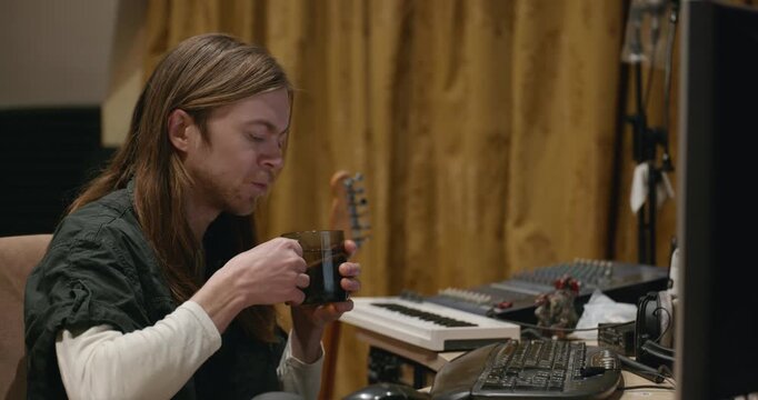 Caucasian man drink hot water in home sound recording studio while working. Single male is drinking tea in evening. 4K 10-bit