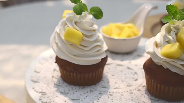 Delicious mango cupcakes topped with rich vanilla whipped cream, fresh diced mango, and mint leaves on a white table. Perfect for tropical dessert, summer baking, or cafe menu concept.