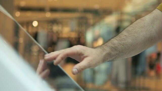 Hand gently taps glass surface. Fingers hover, testing texture. Background blurred, hints at indoor setting. Person appears calm, focused on interaction. Suitable for tech, retail