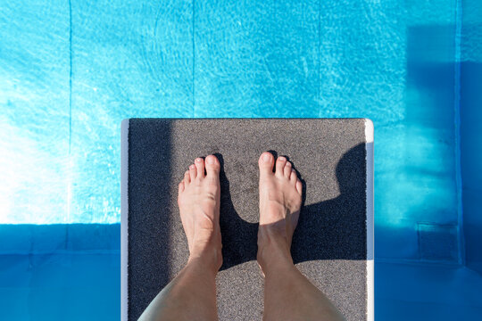 Woman feet on diving board above blue pool water
