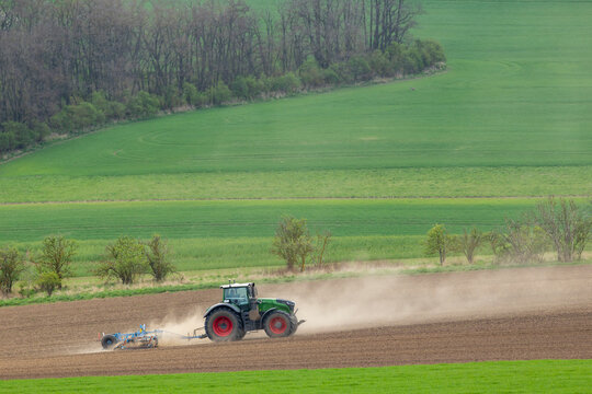 Green tractor cultivating dusty field in Jihomoravsky kraj