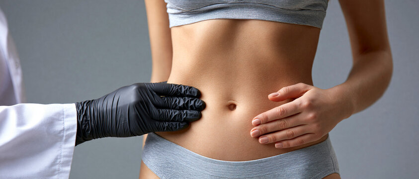 Lipoaspira&ccedil;&atilde;o e contorno corporal. Doutor examinando a barriga de uma jovem paciente de roupa &iacute;ntima cinza. Medicina est&eacute;tica e sa&uacute;de