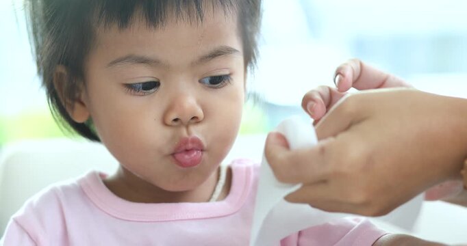 Parent gently wiping a young child mouth with tissue, childcare, family care, hygiene, parenting, cleanliness, health, and everyday caregiving