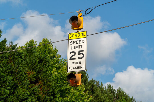 School Speed Limit 25 MPH When Flashing Sign with Amber Lights Against Blue Sky & Green Trees - Road Safety & Student Protection