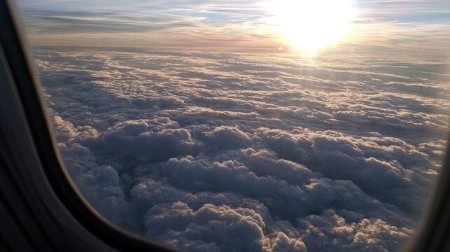 Sunlight glints off fluffy clouds seen from an airplane window at sunrise