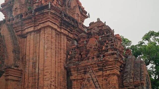 Nha Trang Vietnam. Ancient red brick temple towers with ornate carved pinnacles and conical spire, low-angle view under overcast sky, showing