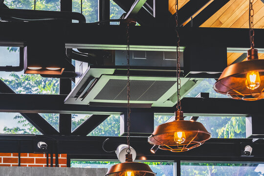 Modern cassette type air conditioner installed on loft ceiling with steel beams and wooden roof. Ceiling-mounted cassette air conditioning unit integrated into modern interior design. HVAC systems.