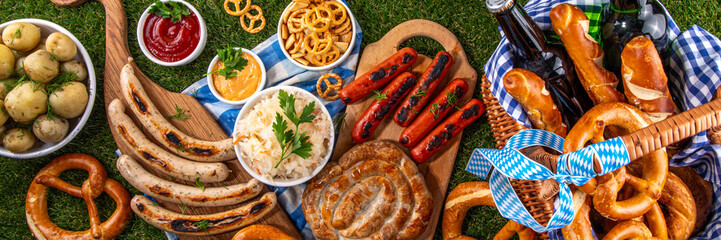 Fototapeta premium Oktoberfest picnic and barbecue food, bavarian party menu, bavarian sausages, pretzels, potato, sauerkraut, beer bottles, with picnic basket, checkered napkin tablecloth, Oktoberfest festive ribbon