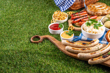 Fototapeta premium Oktoberfest picnic and barbecue food, bavarian party menu, bavarian sausages, pretzels, potato, sauerkraut, beer bottles, with picnic basket, checkered napkin tablecloth, Oktoberfest festive ribbon