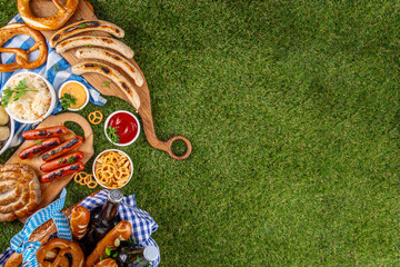 Fototapeta premium Oktoberfest picnic and barbecue food, bavarian party menu, bavarian sausages, pretzels, potato, sauerkraut, beer bottles, with picnic basket, checkered napkin tablecloth, Oktoberfest festive ribbon
