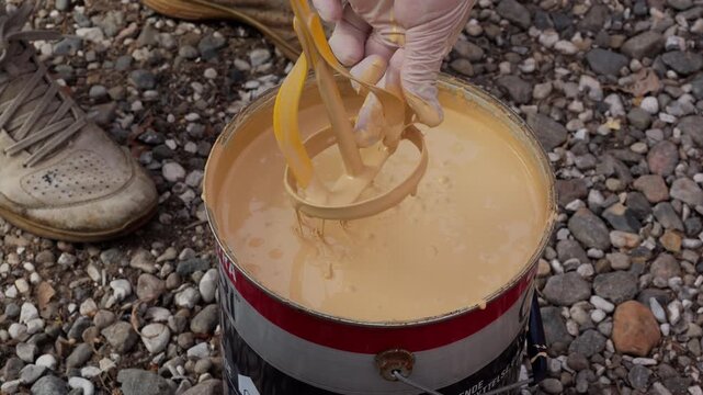 Worker mixing yellow paint with power drill mixer