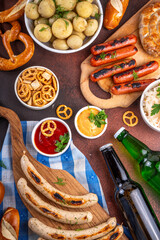 Fototapeta premium Oktoberfest picnic and barbecue food, bavarian party menu, bavarian sausages, pretzels, potato, sauerkraut, beer bottles, with picnic basket, checkered napkin tablecloth, Oktoberfest festive ribbon