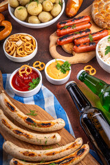 Fototapeta premium Oktoberfest picnic and barbecue food, bavarian party menu, bavarian sausages, pretzels, potato, sauerkraut, beer bottles, with picnic basket, checkered napkin tablecloth, Oktoberfest festive ribbon