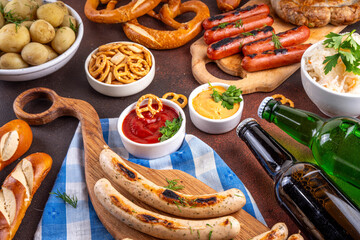 Fototapeta premium Oktoberfest picnic and barbecue food, bavarian party menu, bavarian sausages, pretzels, potato, sauerkraut, beer bottles, with picnic basket, checkered napkin tablecloth, Oktoberfest festive ribbon