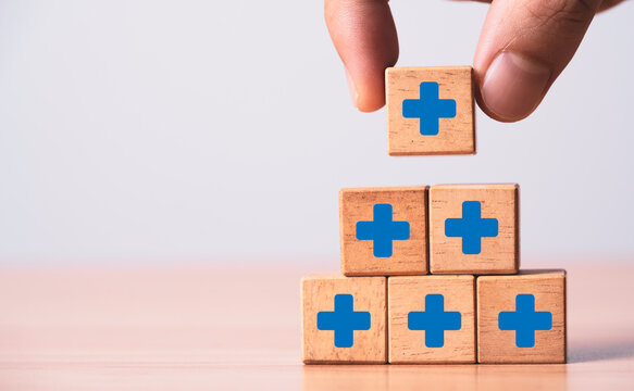 Hand placing a plus symbol block onto a pyramid, representing positive mindset, personal growth, mental wellness, self-improvement, resilience, confidence, motivation and success.