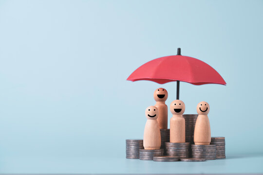Wooden family figures protected by a red umbrella with stacked coins, symbolizing financial security, life insurance, family protection, savings, wealth planning and long-term financial stability.