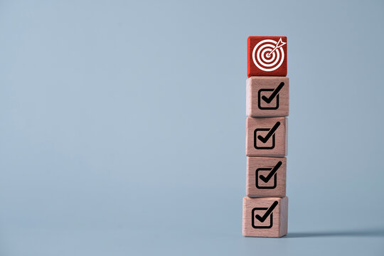 Stacked wooden checklist progress blocks leading to a target icon for goal achievement, strategic planning, task completion, project management, business success, productivity and milestone tracking.