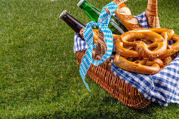 Fototapeta premium Oktoberfest picnic and barbecue food, bavarian party menu, bavarian sausages, pretzels, potato, sauerkraut, beer bottles, with picnic basket, checkered napkin tablecloth, Oktoberfest festive ribbon