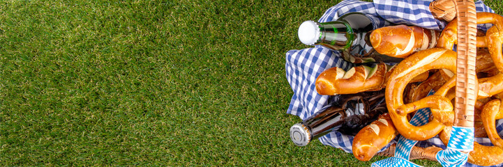 Fototapeta premium Oktoberfest picnic and barbecue food, bavarian party menu, bavarian sausages, pretzels, potato, sauerkraut, beer bottles, with picnic basket, checkered napkin tablecloth, Oktoberfest festive ribbon