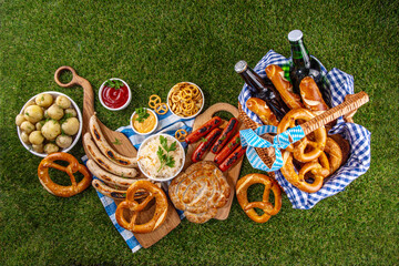 Fototapeta premium Oktoberfest picnic and barbecue food, bavarian party menu, bavarian sausages, pretzels, potato, sauerkraut, beer bottles, with picnic basket, checkered napkin tablecloth, Oktoberfest festive ribbon