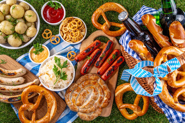 Fototapeta premium Oktoberfest picnic and barbecue food, bavarian party menu, bavarian sausages, pretzels, potato, sauerkraut, beer bottles, with picnic basket, checkered napkin tablecloth, Oktoberfest festive ribbon