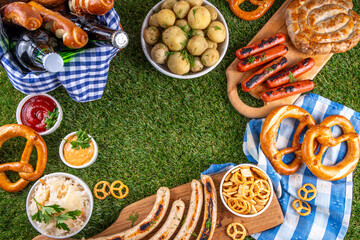 Fototapeta premium Oktoberfest picnic and barbecue food, bavarian party menu, bavarian sausages, pretzels, potato, sauerkraut, beer bottles, with picnic basket, checkered napkin tablecloth, Oktoberfest festive ribbon