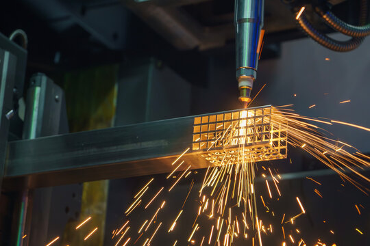 High-precision fiber laser cut machine performing an engraving and cutting process on a square steel pipe with sparkling light.