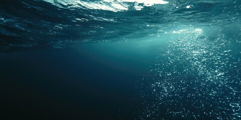 Fototapeta premium Underwater view of sunlight filtering through rippling ocean surface, bubbles rise