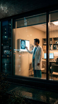 Focused doctor examining a brain scan on a display in a modern clinic seen at night