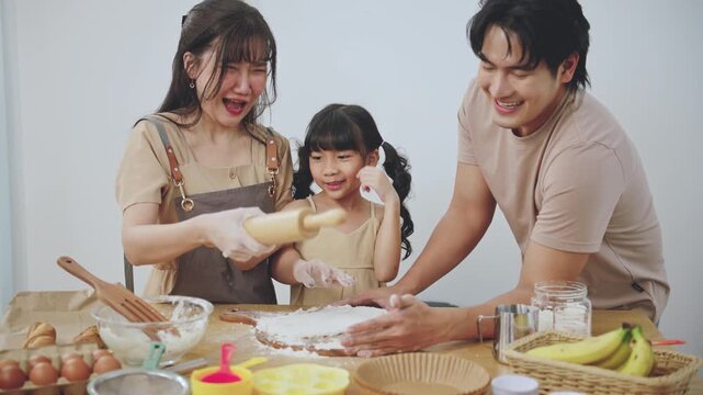 Happy Asian family baking together in kitchen, parents teaching child cooking at home. Concept of parenting, learning activity for kids, family bonding, and home lifestyle.