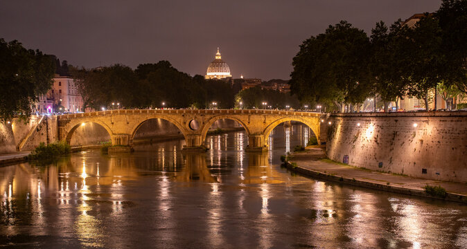 Beautiful illuminated view of Rome, Italy with Saint Peters Basiica, historic architecture, bridges and Tiber River under evening sky. 