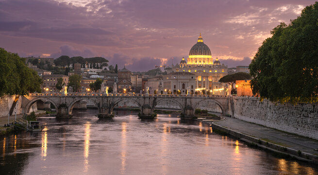 Beautiful illuminated view of Rome, Italy with Saint Peters Basiica, historic architecture, bridges and Tiber River under evening sky. 