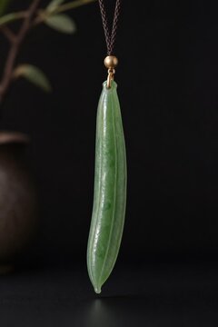 A slender green jade pendant shaped like a silique on a dark background.