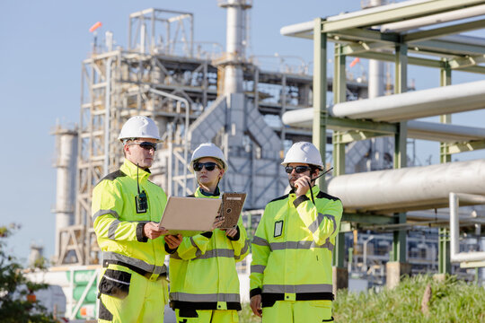Construction engineers wearing safety gear examine blueprints at an industrial site with heavy machinery visible in the background