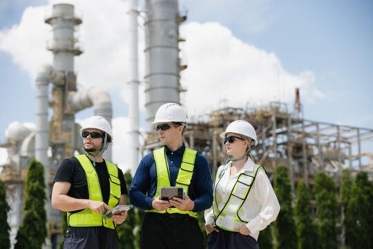 Team of engineers in safety gear collaborating at construction site with industrial equipment in the background
