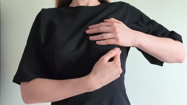 Woman lifts her shirt and palpates her breast checking for lumps with her hands. She performs a careful self examination feeling for changes in her chest. Concept of breast self exam,