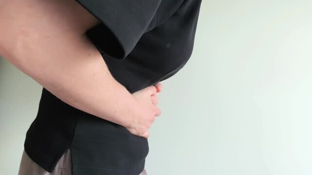 Woman clutches her stomach with both hands experiencing sudden sharp cramps. She bends forward while pressing tightly on her abdomen in pain. Concept of acute stomach cramps, gastric spasm