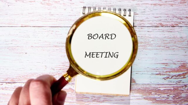 A hand uses a magnifying glass to zoom in on letters on a notepad. The focus shifts to details of a board meeting in an office space