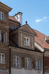 Obraz premium Ancient European architecture features historic tenement house facades with orange tile roofs. Open windows and a decorative gable stand under a clear blue sky in a scenic urban setting.