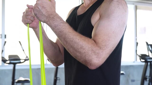 Close-up of a man training with resistance bands in a gym, building arm strength, muscle and endurance through functional fitness exercises.