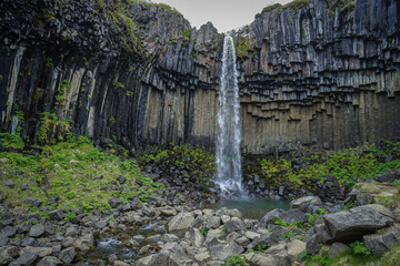 A waterfall cascades through hexagonal basalt columns in a rugged, moss-covered landscape,Svartifoss,Iceland © SHUNJI ZHOU
