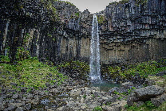 A waterfall cascades through hexagonal basalt columns in a rugged, moss-covered landscape,Svartifoss,Iceland
