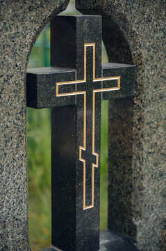 serene grave marker with cross in granite cemetery close-up with black and gold accents, solemn and peaceful setting for religious memorial use cases and editorial content.