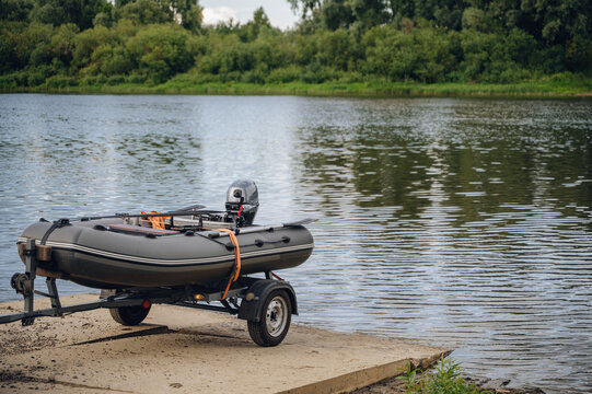 inflatable boat on lakeside trailer with calm water and oars visible, side view, rubber, metal, plastic, serene boating scene, modern outdoor activities, clean background, copyspace.
