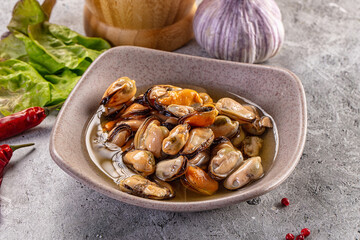 Fototapeta premium Cooked mussels in ceramic bowl with garlic and chili peppers on stone surface