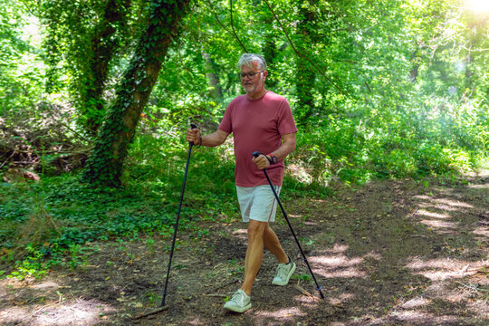 Senior man enjoying Nordic walking through a forest trail to improve cardiovascular fitness, balance, endurance, mobility, and support an active healthy lifestyle.