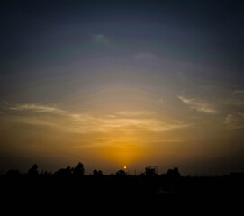 Fototapeta premium Vibrant sunset casting a warm glow over a dark silhouette of trees